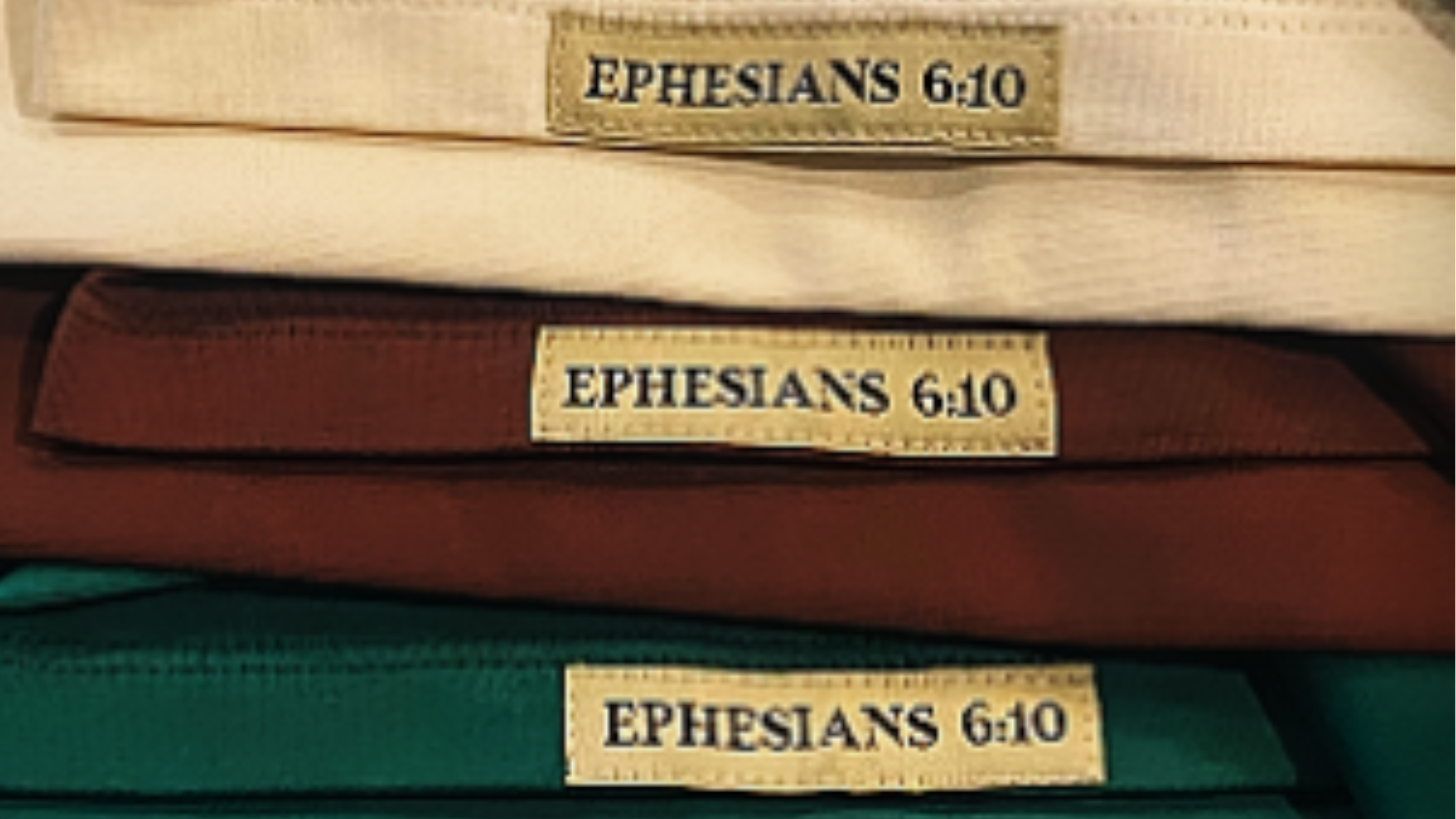 Folded t-shirts from The Meek Collection by THE ARMOR OF GOD™ in cream brown and green with visible Ephesians 6 10 woven labels.